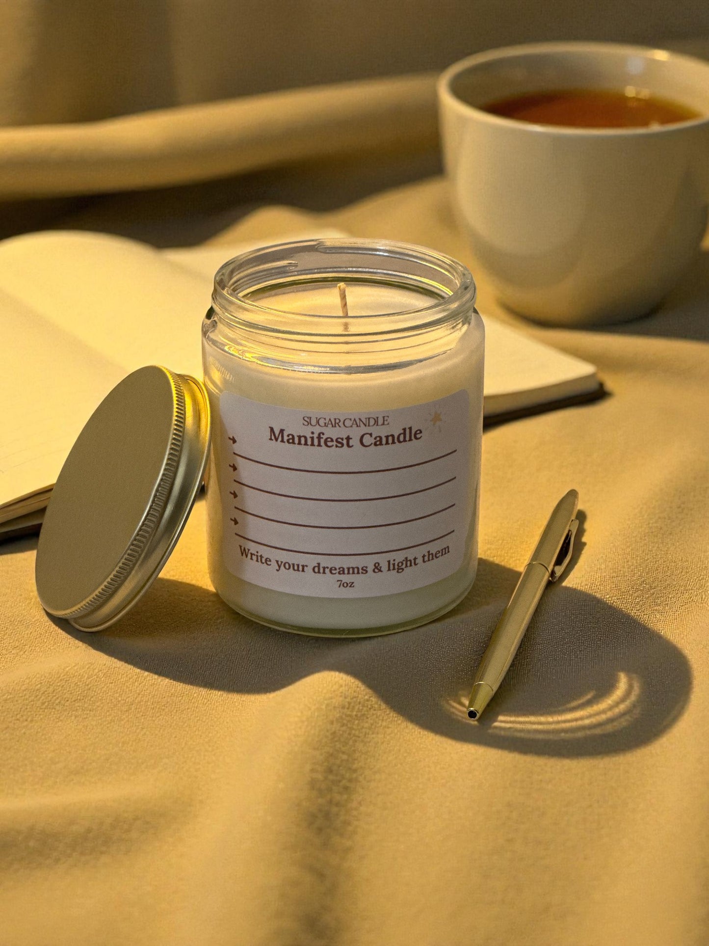 Jar of 'Manifest Candle' with a pen and notebook on a textured surface