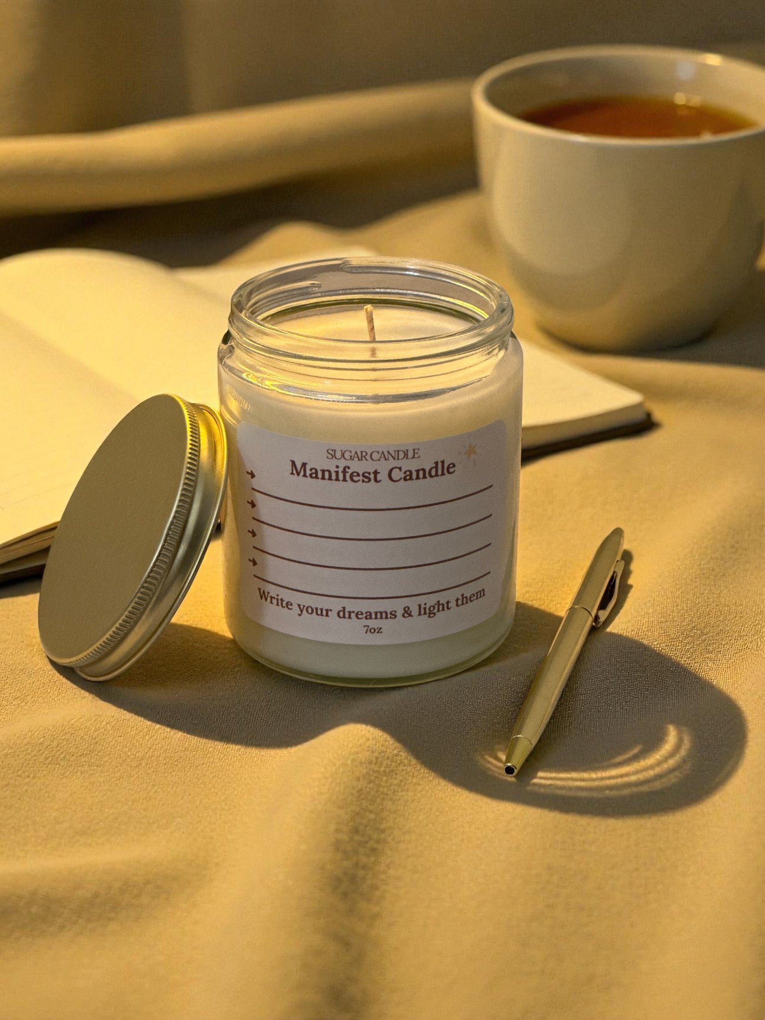 Jar of 'Manifest Candle' with a pen and notebook on a textured surface