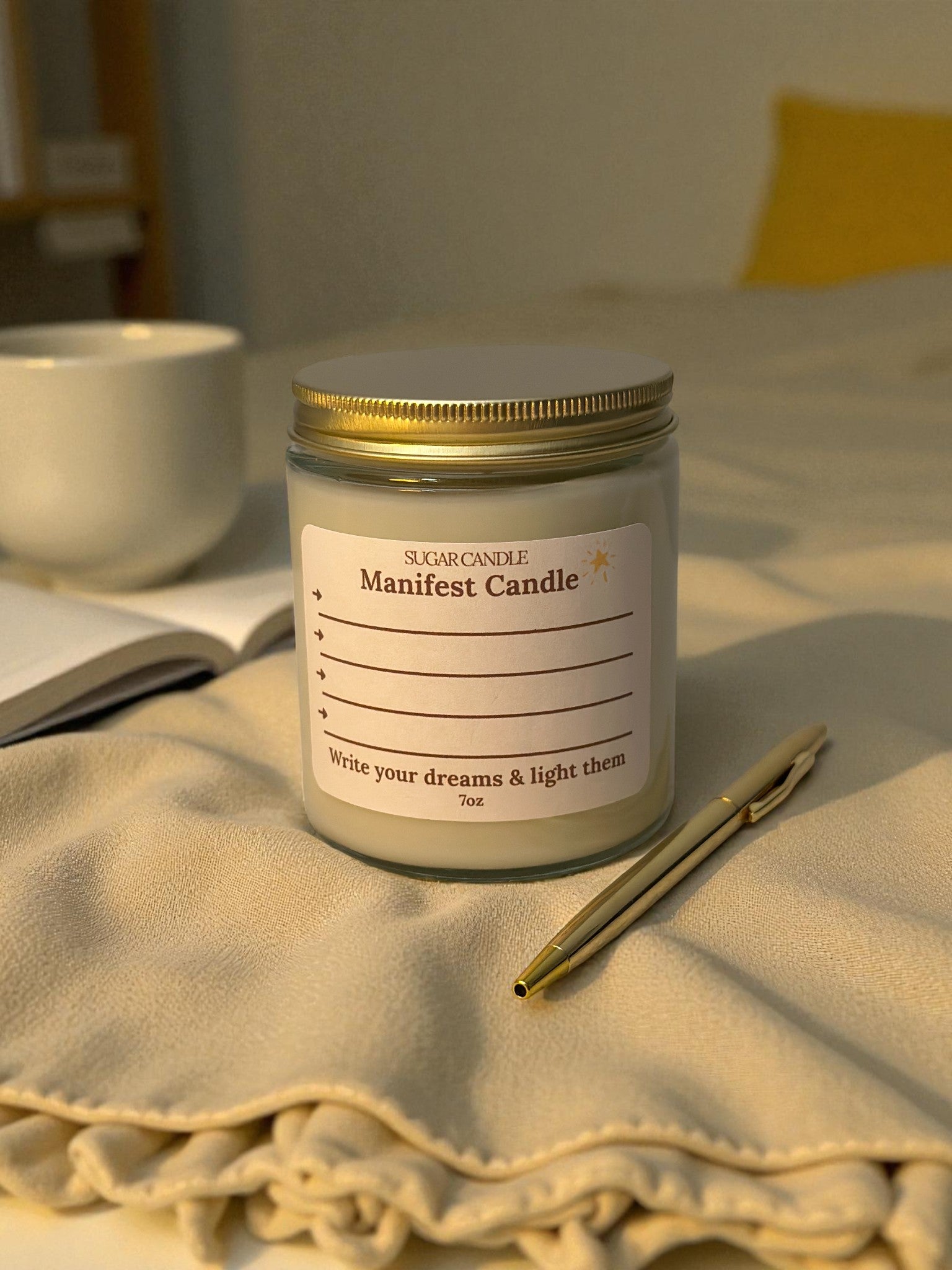 Manifest candle with a label on a blanket next to a pen and notebook