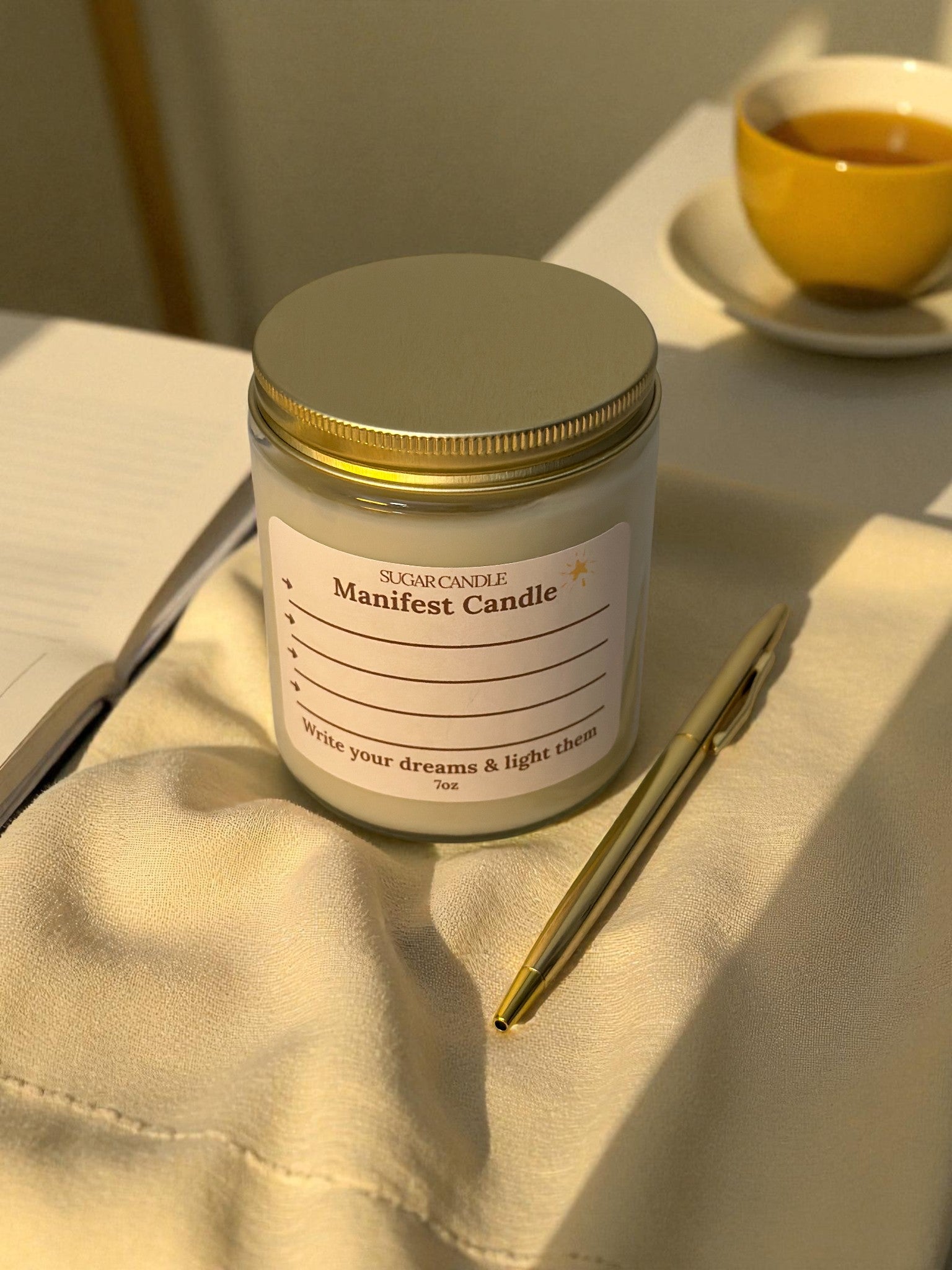 Manifest candle jar with a label on a surface with a pen and cup in the background