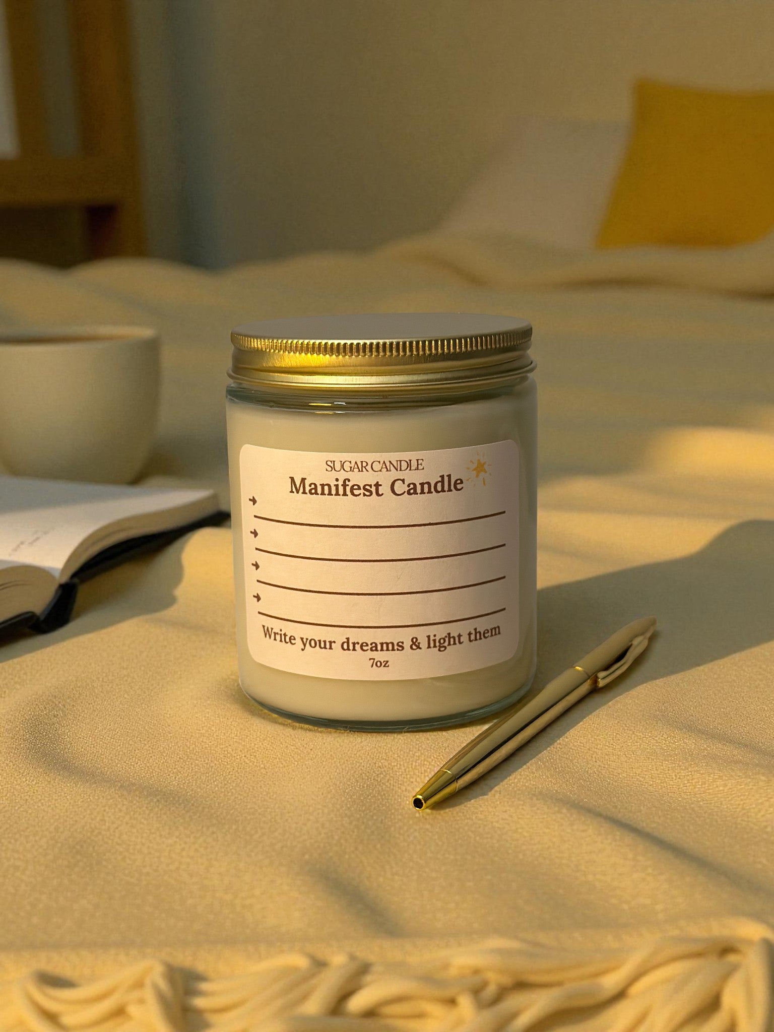 Manifest candle with a label on a soft surface, surrounded by a pen and a cup.