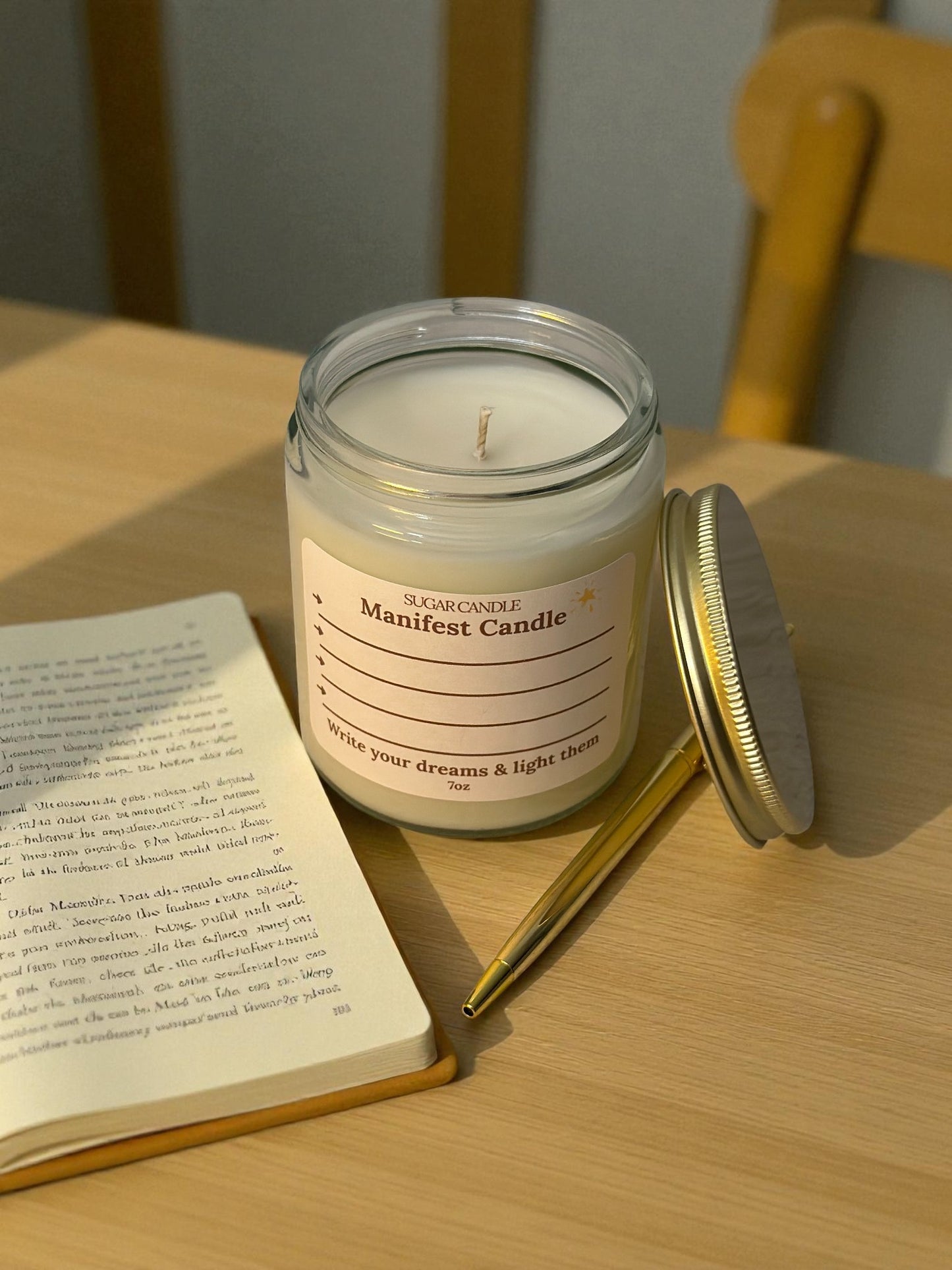 Manifestation candle with a label on a wooden table next to an open book and pen