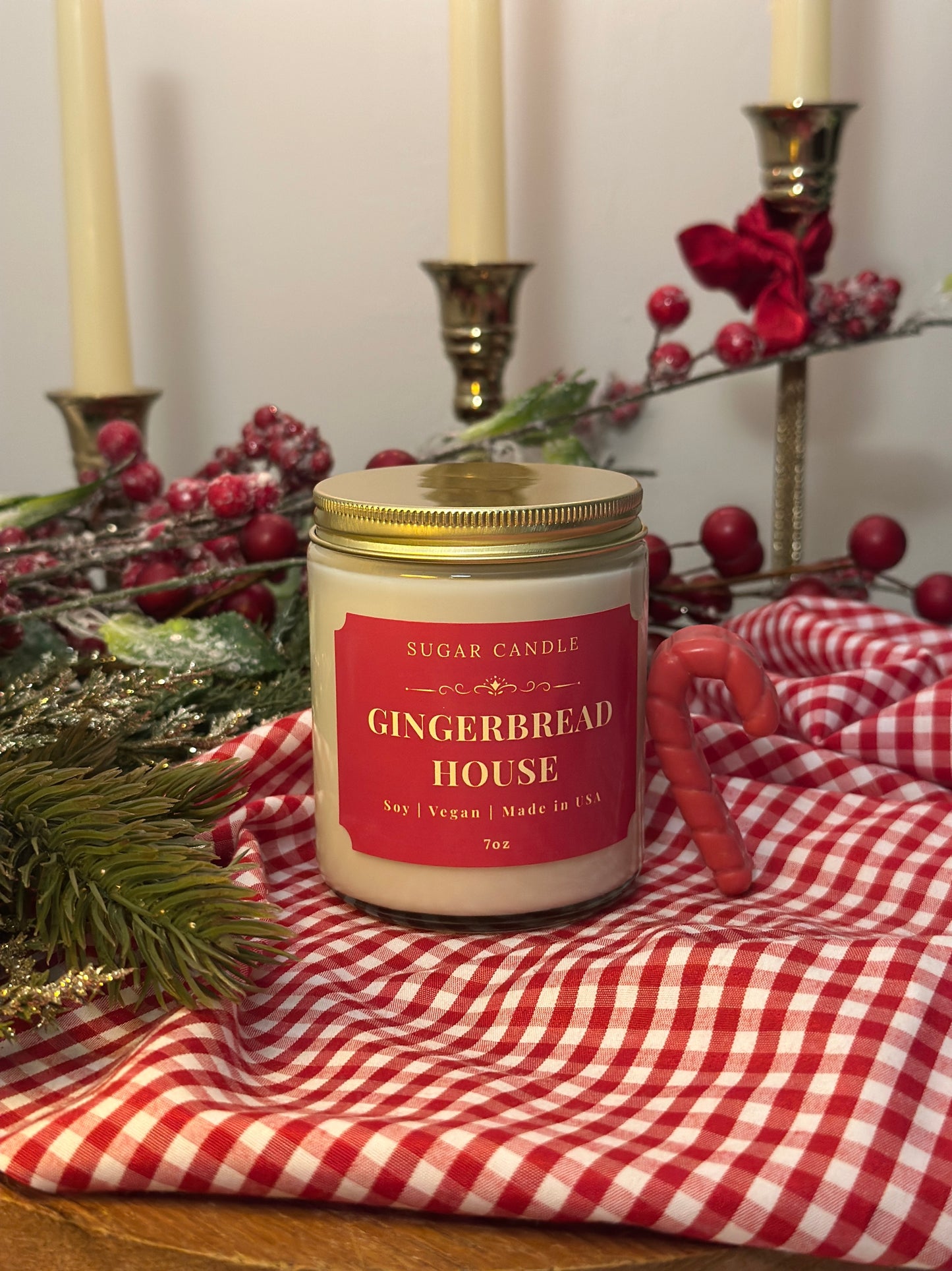 Gingerbread house candle on a red and white checkered tablecloth with Christmas decorations.