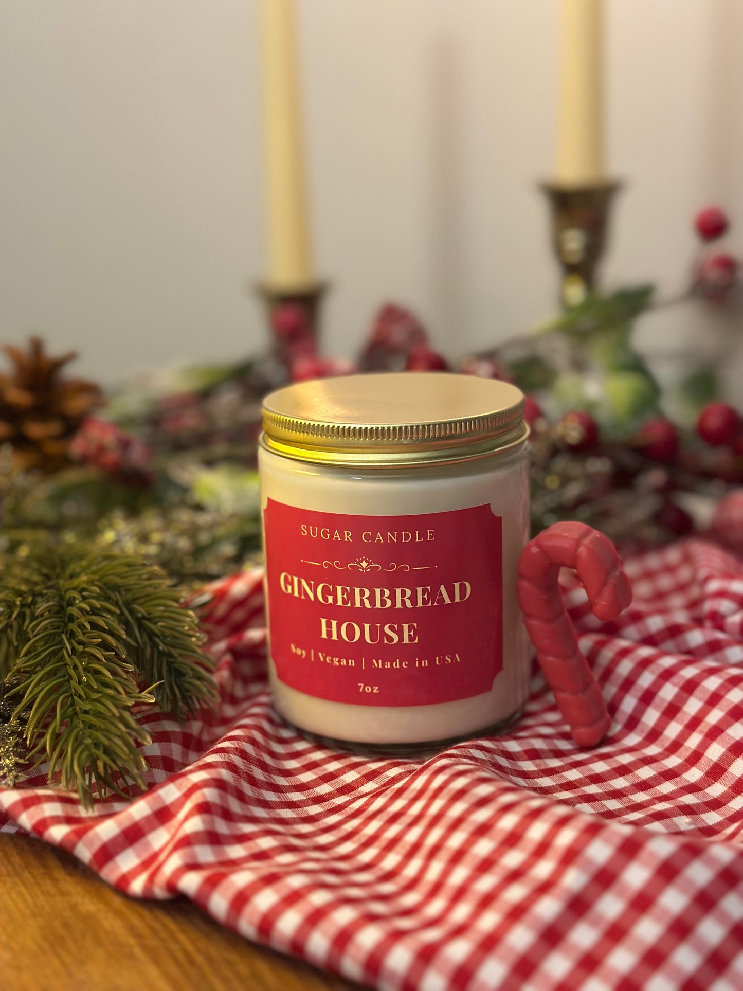 Gingerbread house candle on a checkered cloth with Christmas decorations in the background