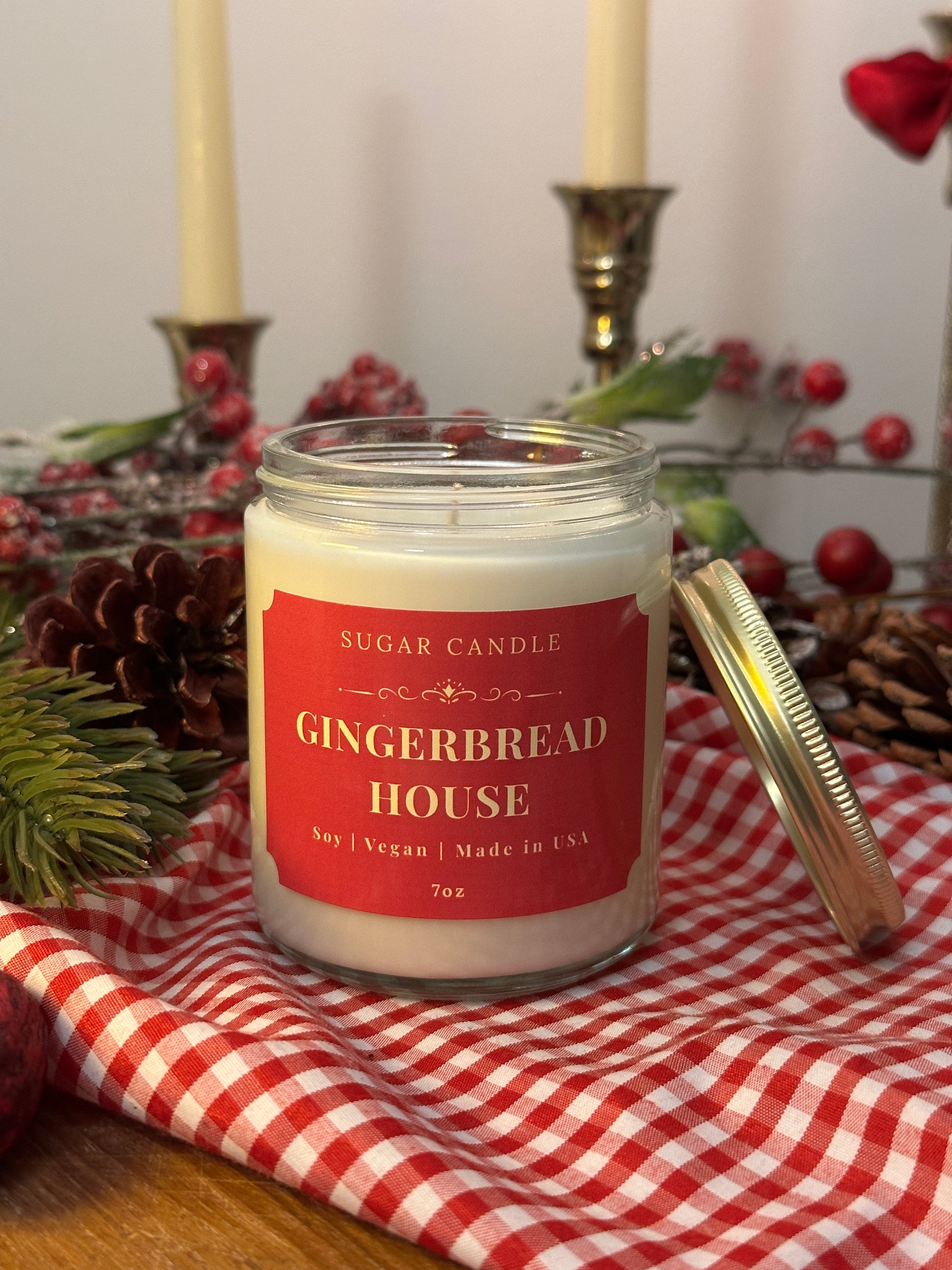 Gingerbread House candle with a red label on a checkered cloth with Christmas decorations.
