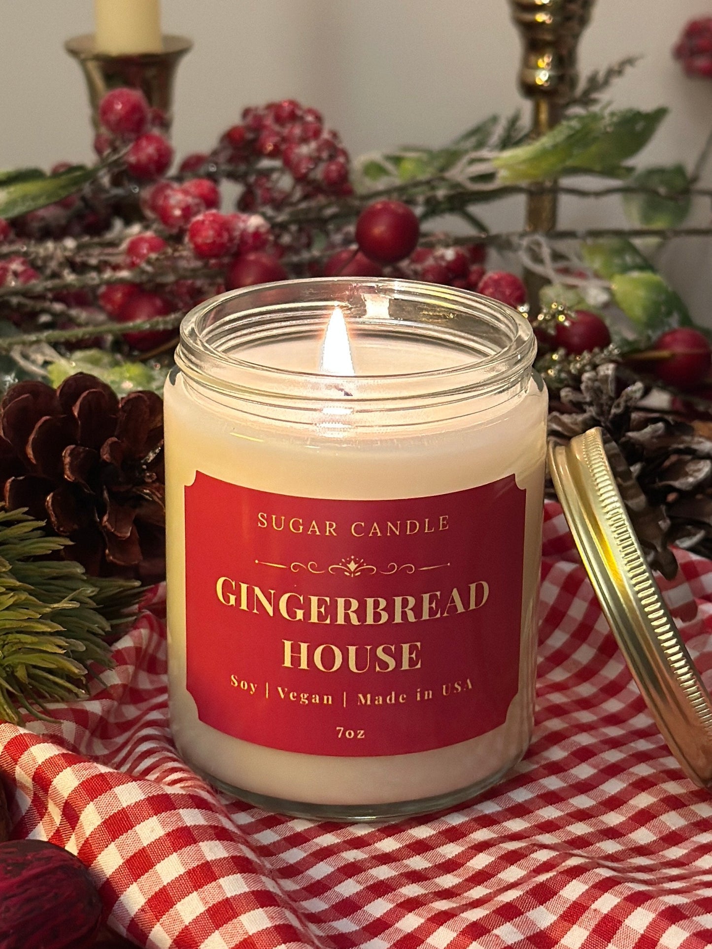 Candle labeled 'Gingerbread House' on a checkered cloth with festive decorations in the background.