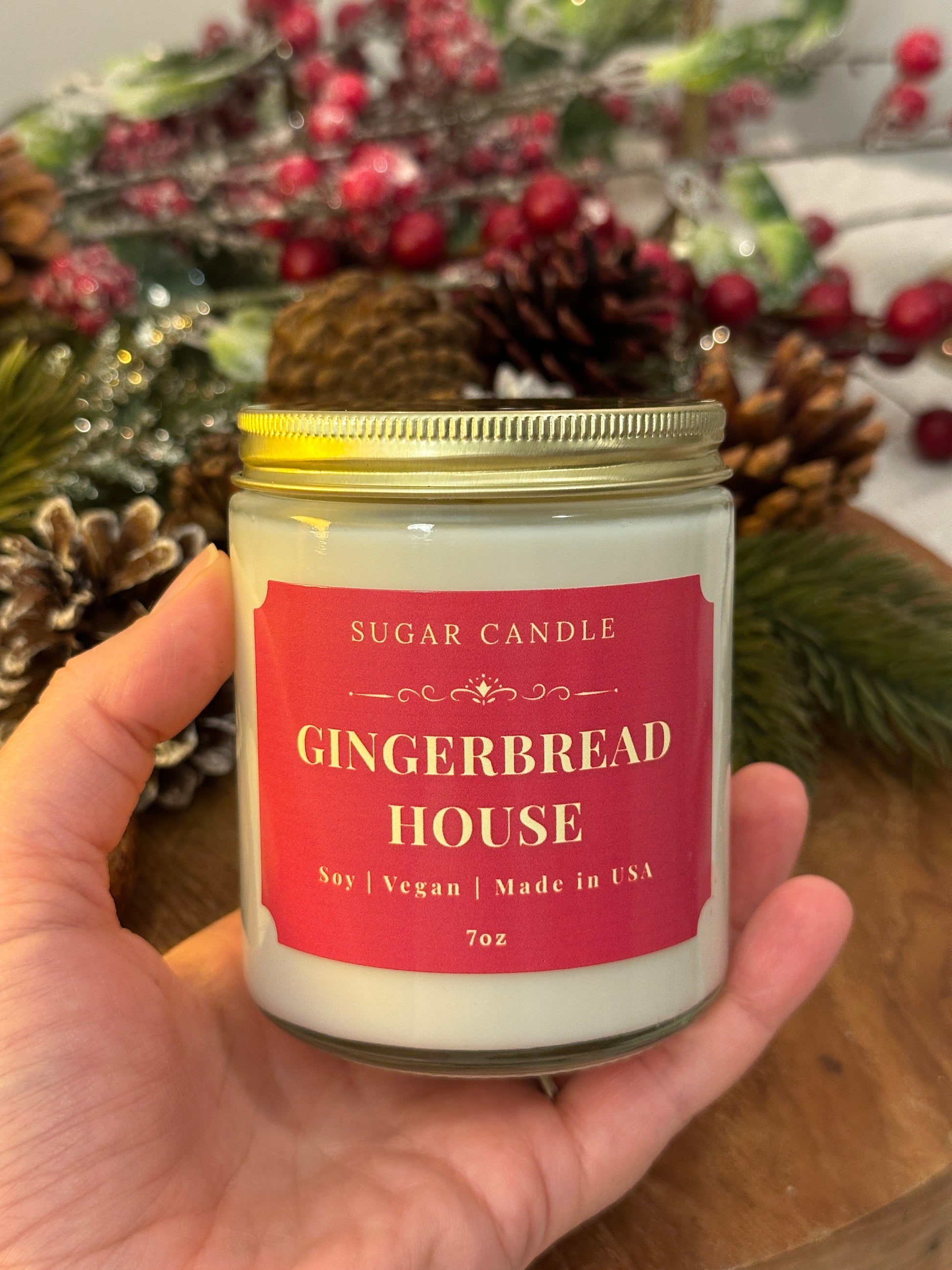Hand holding a 'Gingerbread House' candle with a festive background