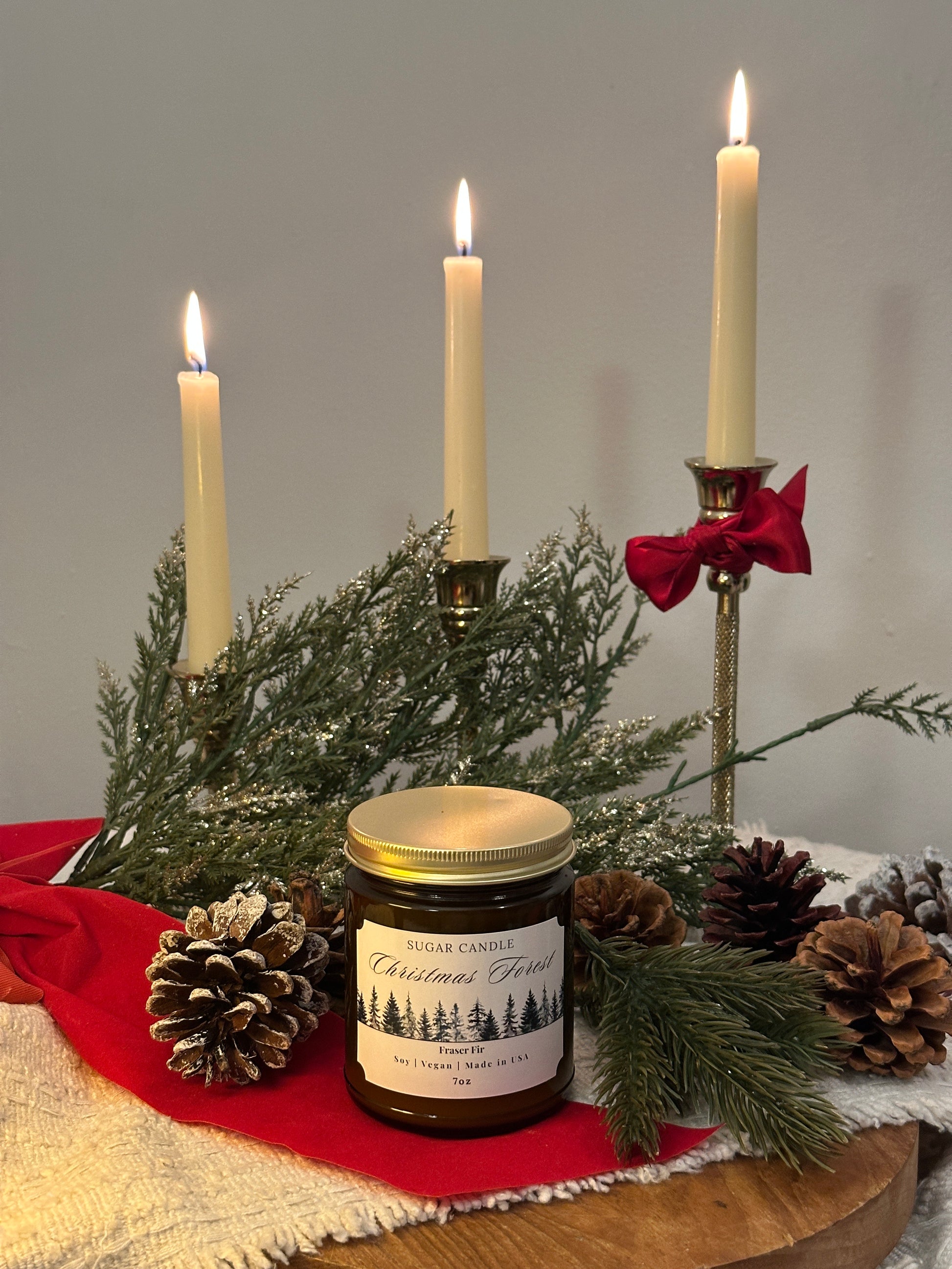 Candlelit scene with a jar of jam, pinecones, and greenery on a red cloth.