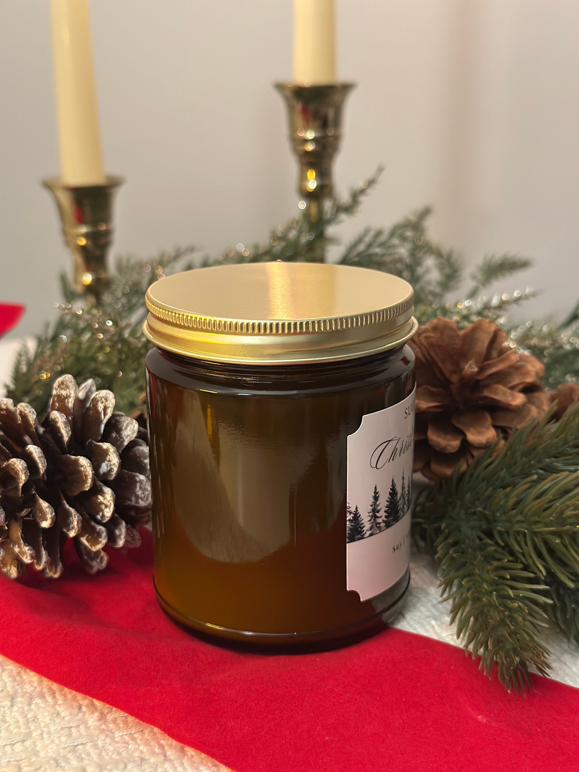 Jar with a gold lid on a red surface with pine cones and greenery