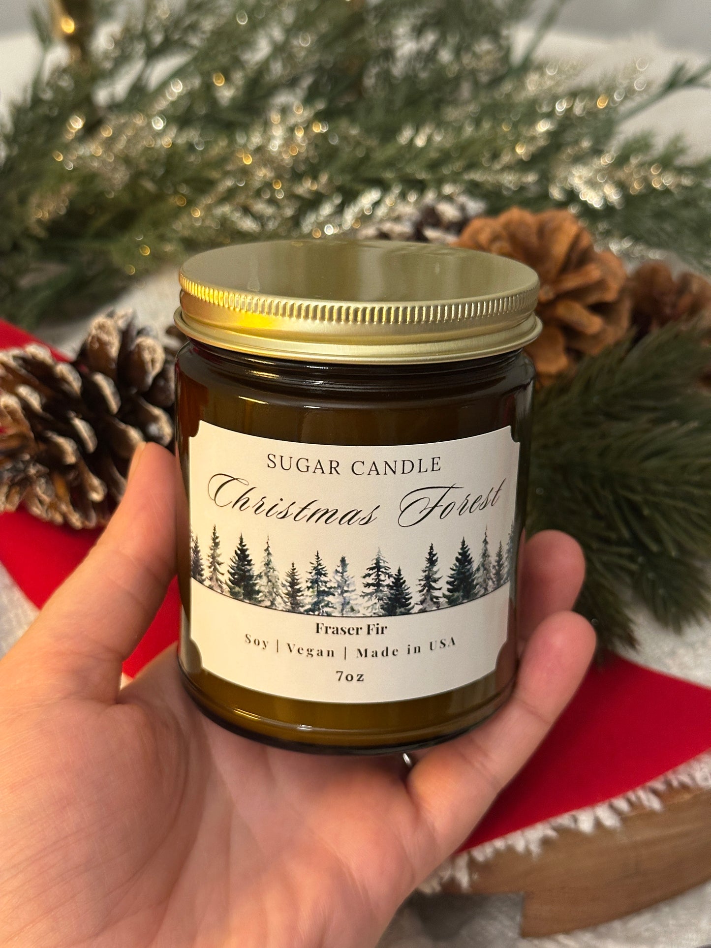 Hand holding a candle labeled 'Christmas Forest' with decorative background