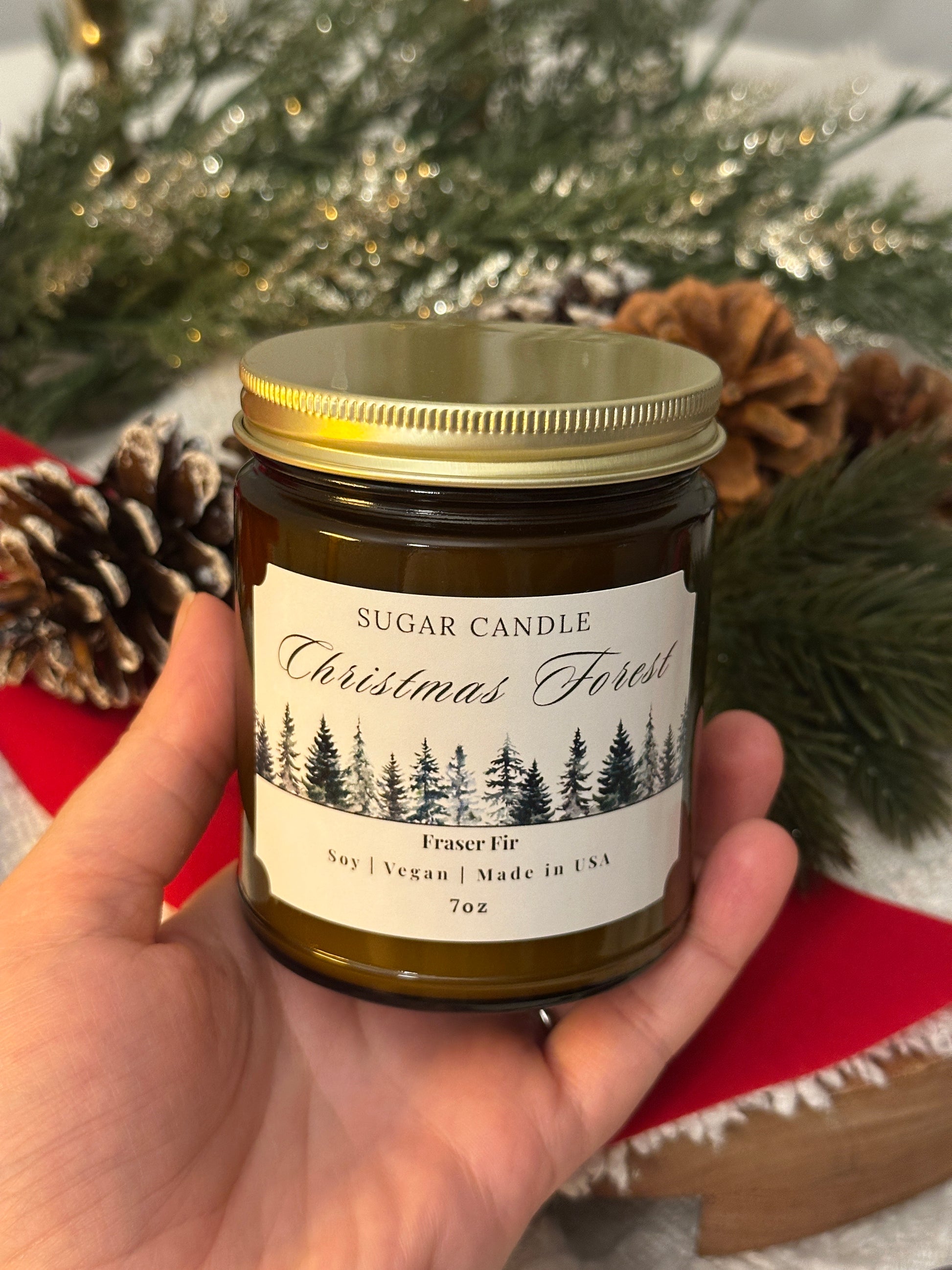 Hand holding a candle labeled 'Christmas Forest' with decorative background