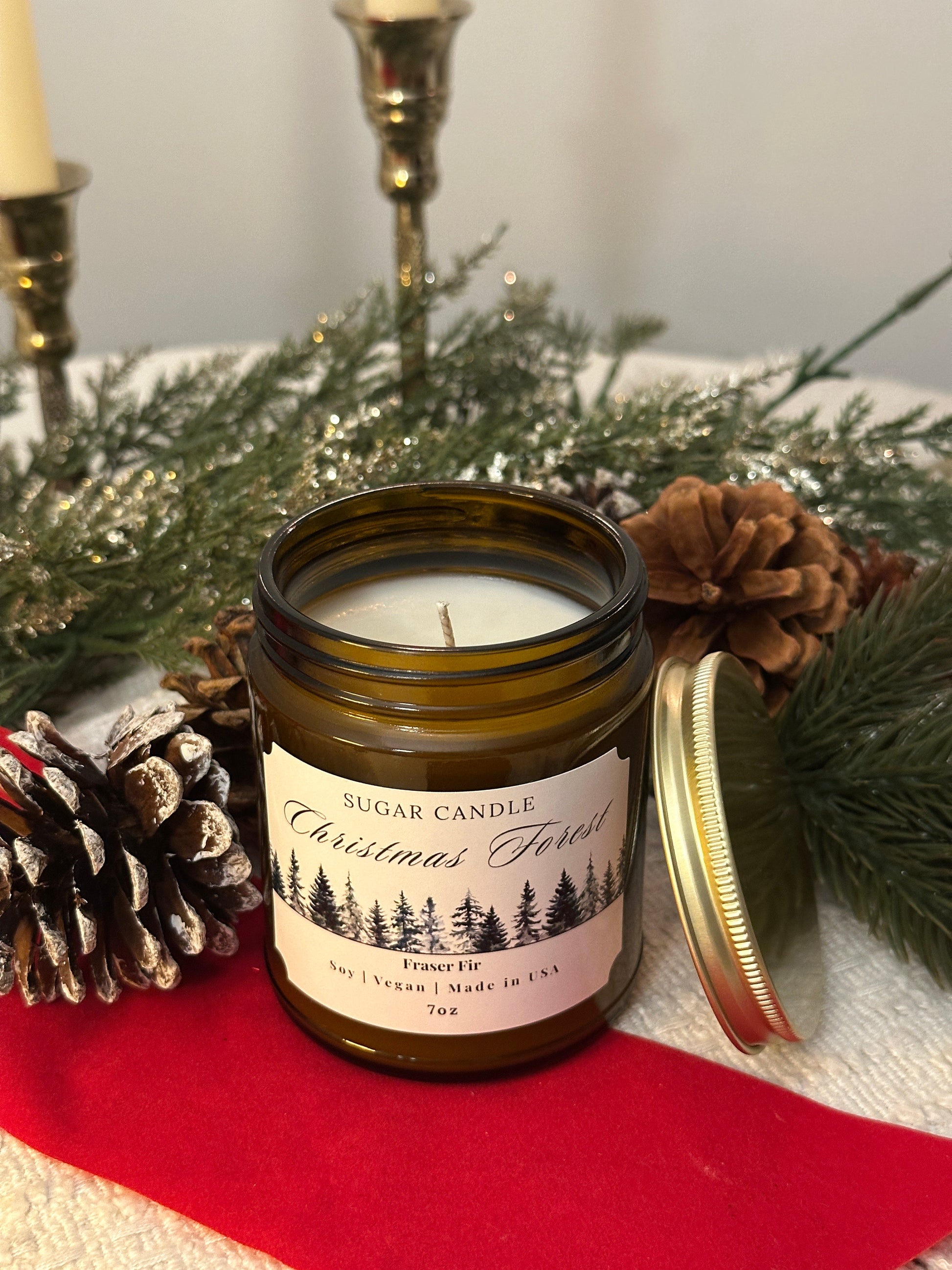 Jar candle with decorative label on a surface with pine cones and greenery