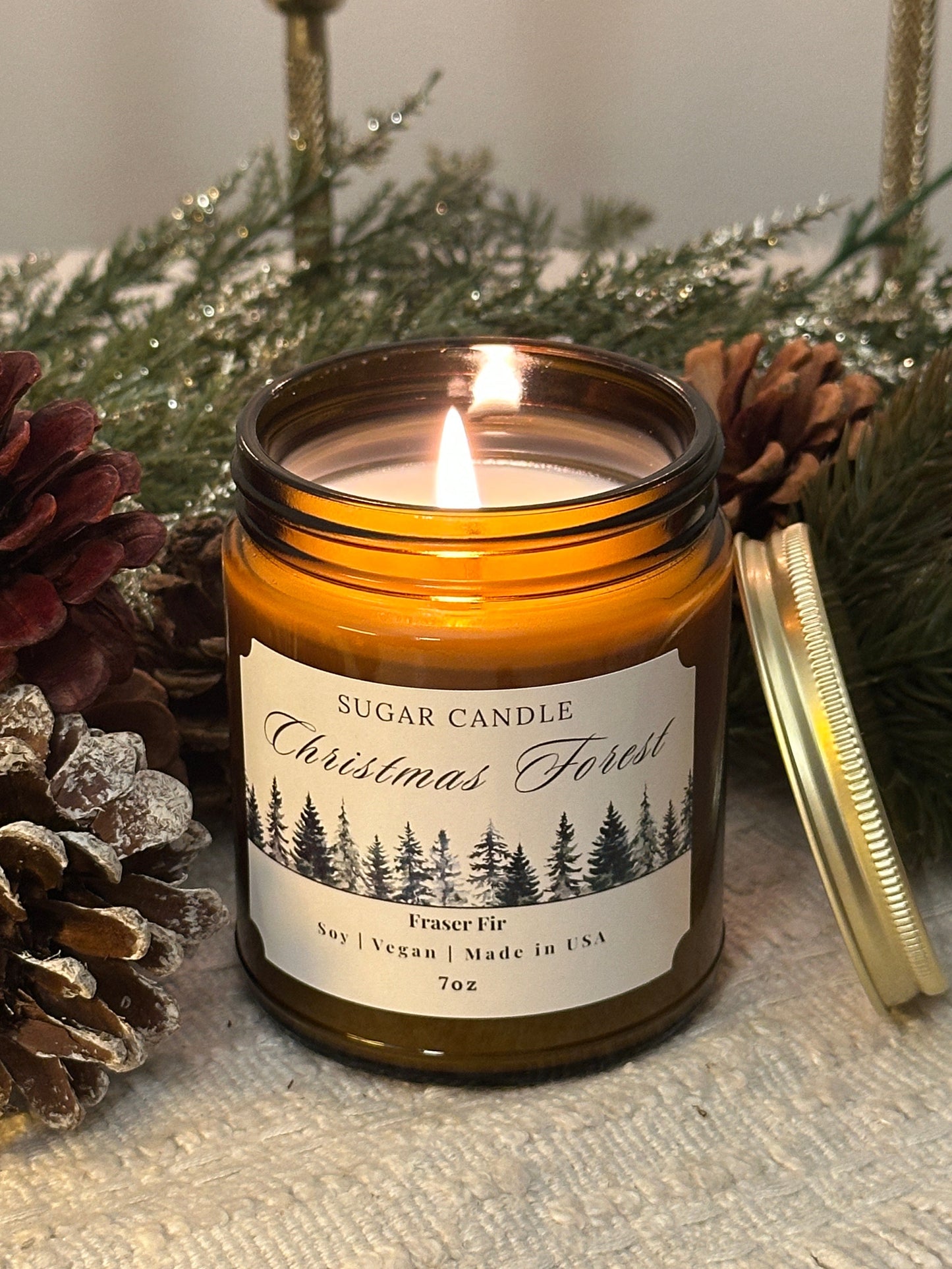 Candle in a jar with a label on a decorative surface with pine cones and greenery
