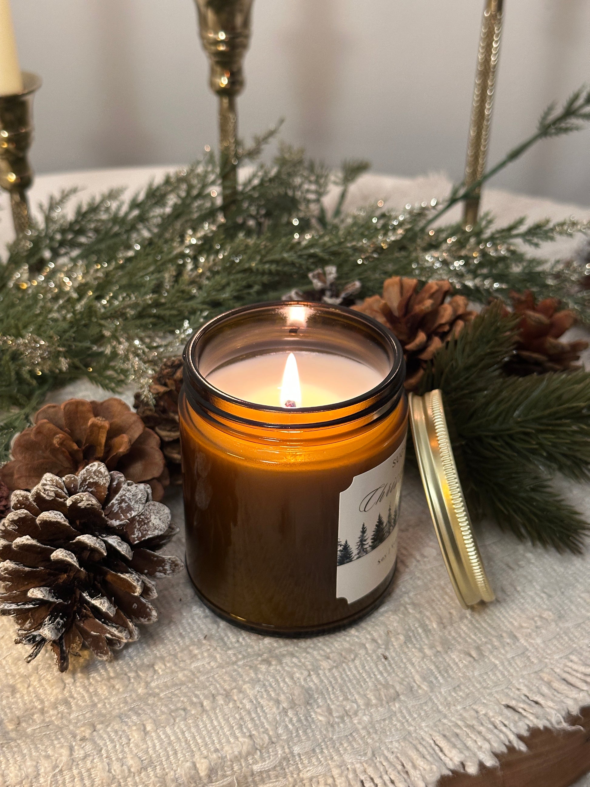 Candle in a jar with a label on a decorative surface with pine cones and greenery