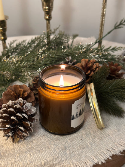 Candle in a jar with a label on a decorative surface with pine cones and greenery