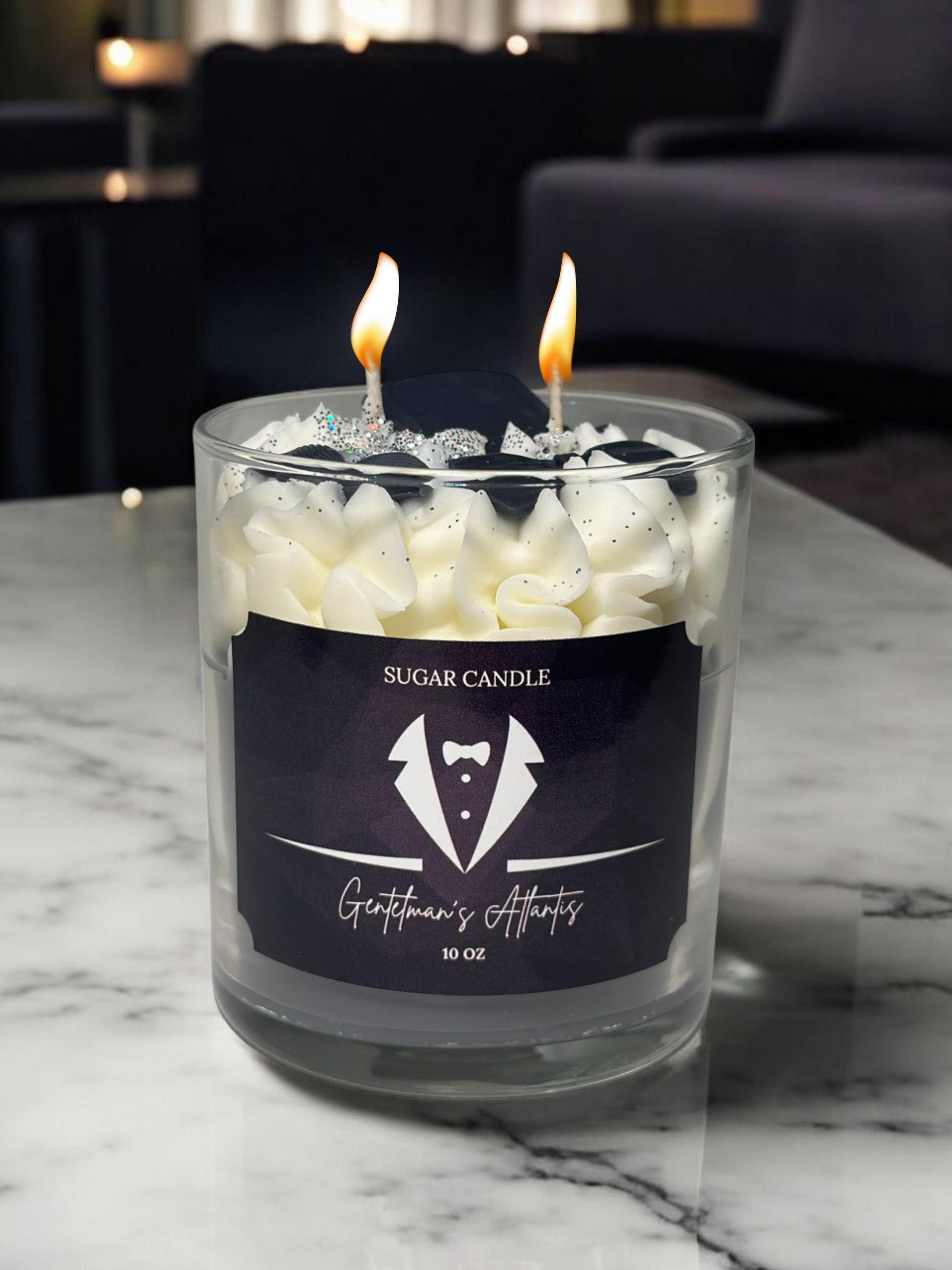 Glass candle with two lit wicks on a marble surface, featuring a label for 'Sugar Candle' and 'Gentleman's Attire'.