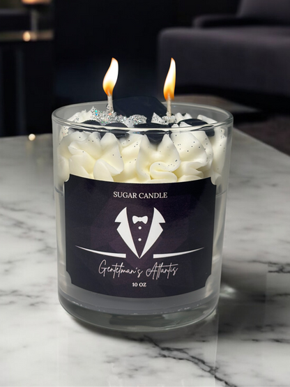 Glass candle with two lit wicks on a marble surface, featuring a label for 'Sugar Candle' and 'Gentleman's Attire'.