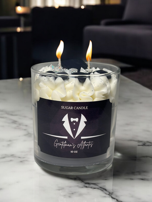 Glass candle with two lit wicks on a marble surface, featuring a label for 'Sugar Candle' and 'Gentleman's Attire'.