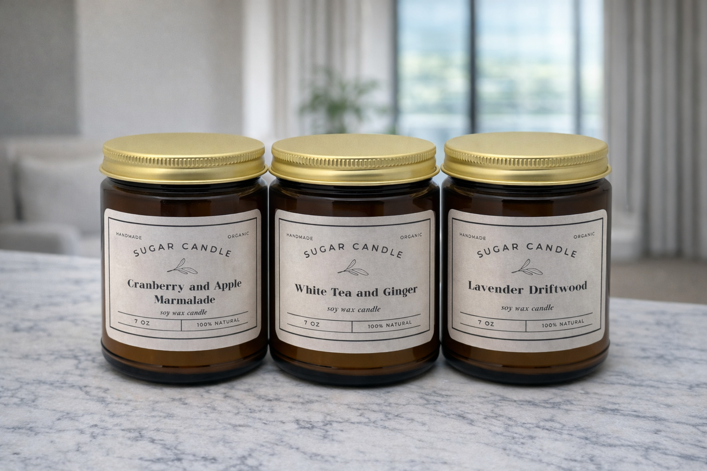 Three candles with gold lids on a marble surface, labeled 'Cranberry and Apple Marmalade', 'White Tea and Ginger', and 'Lavender Driftwood'.