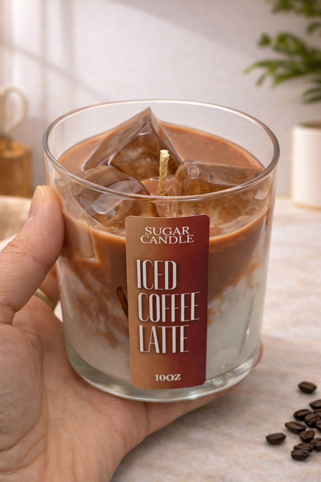 Candle labeled 'Iced Coffee Latte' held by a hand with coffee beans on a surface.