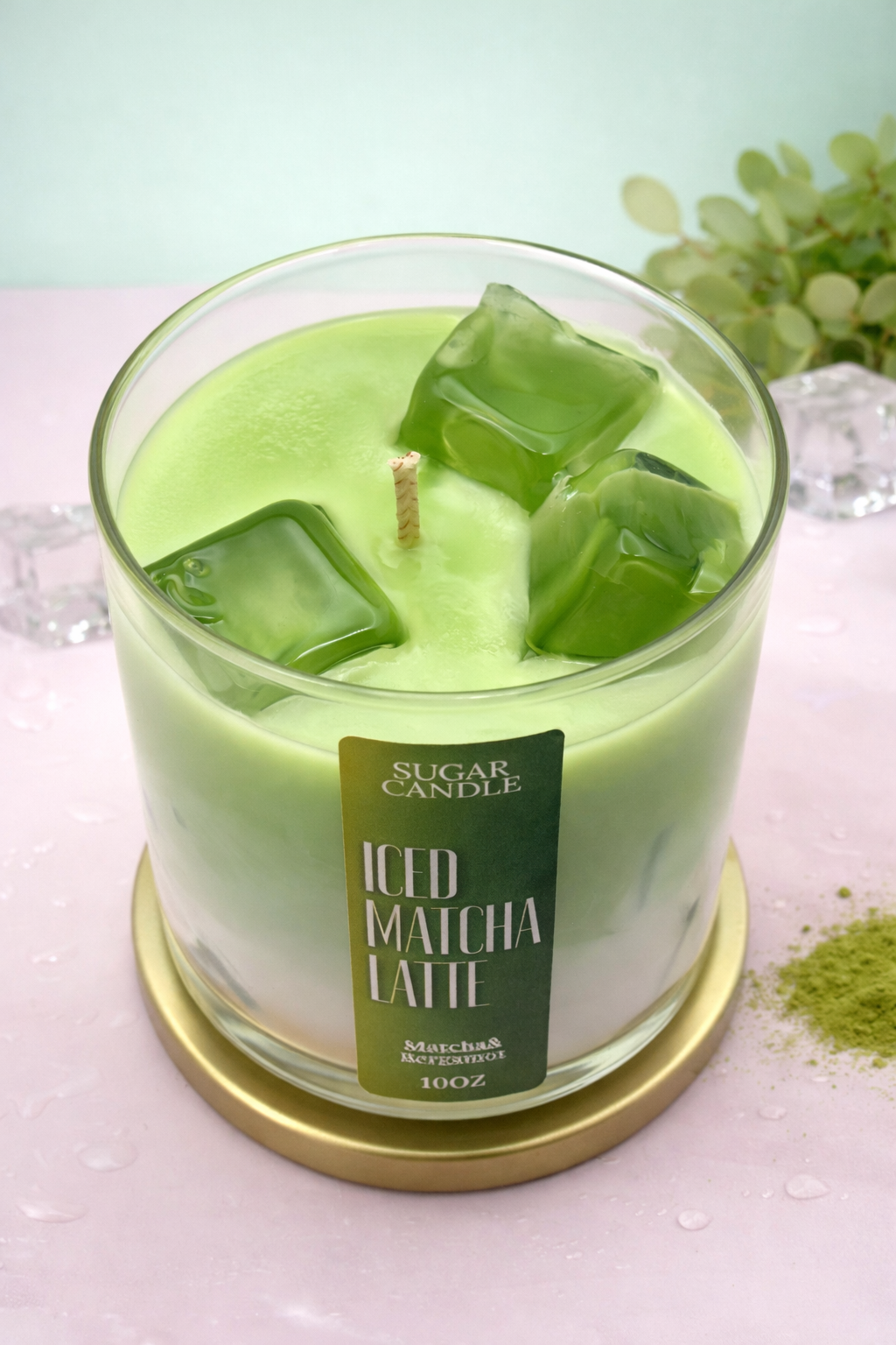 Green candle labeled 'ICED MATCHA LATTESUGAR CANDLE' with a gold coaster on a light background.