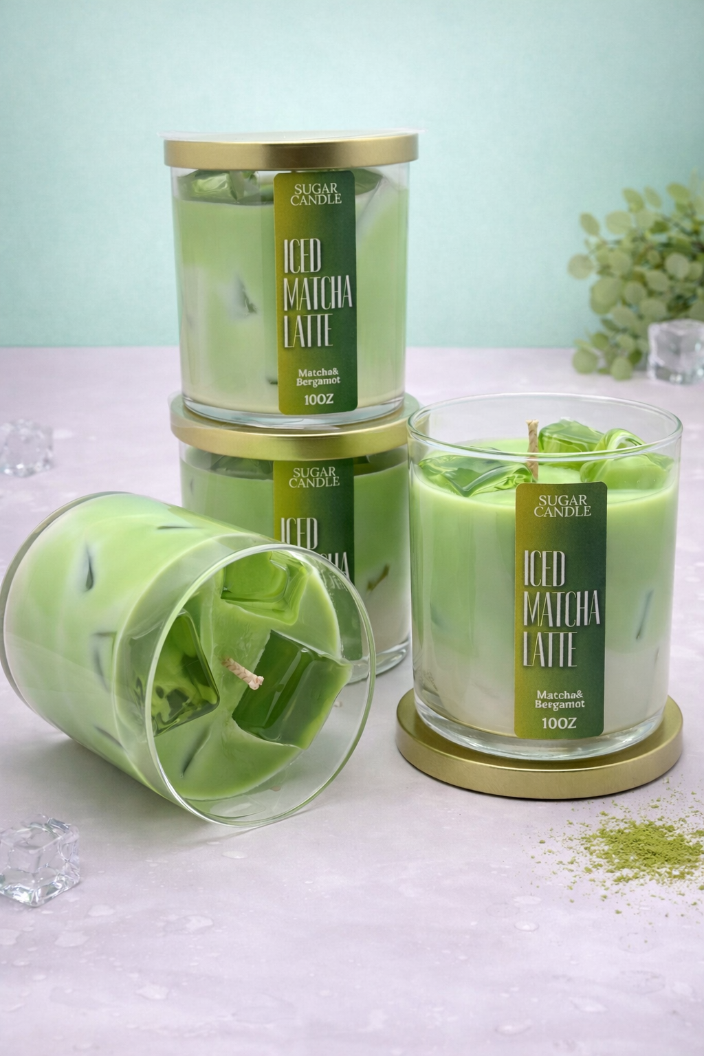 Green iced matcha latte candles with gold lids on a light surface.