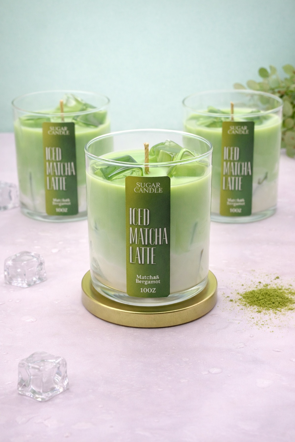 Green candle labeled 'Iced Matcha Latte' on a white surface with matcha powder and ice cubes.